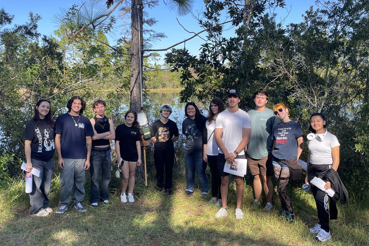 A group of 11 men and women pose among trees on sunny day
