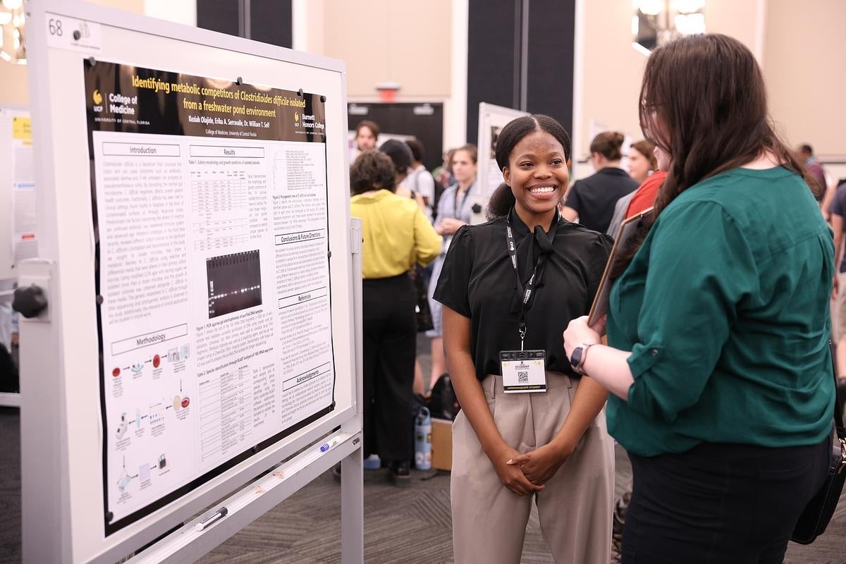 A student presenting to someone while standing in front of a research poster