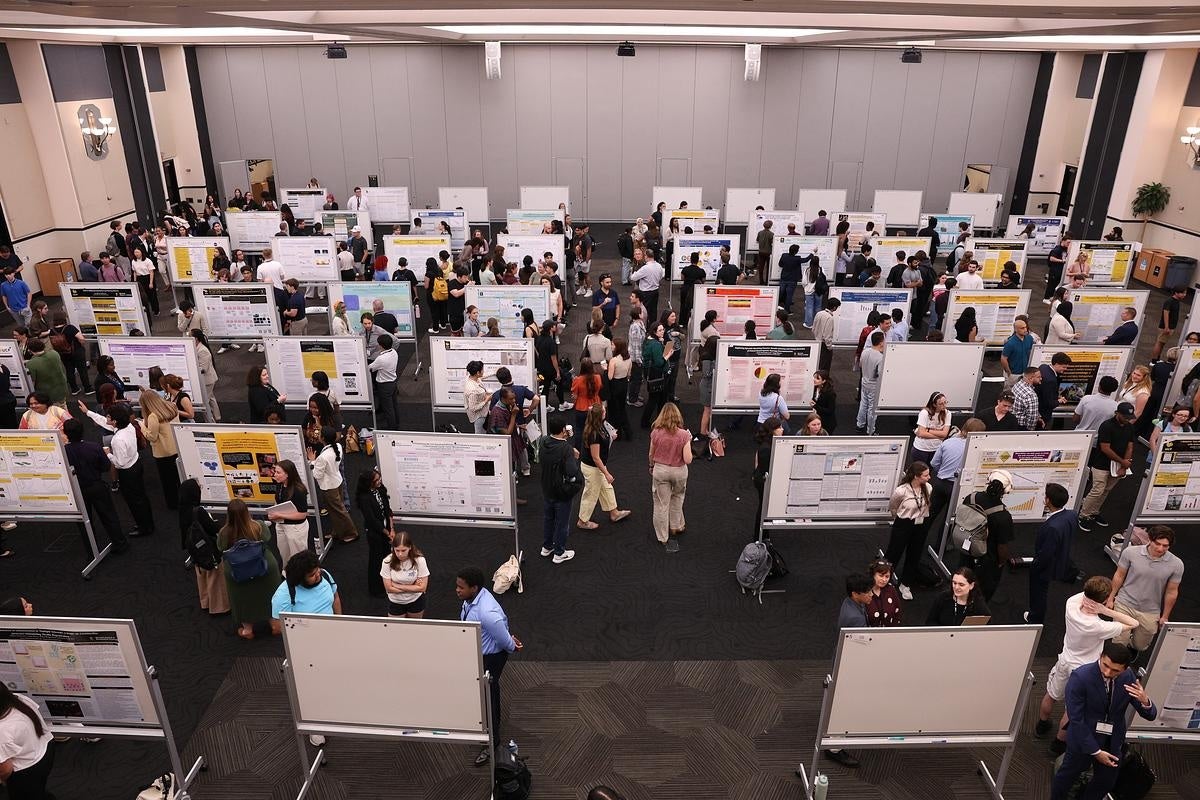 An aerial view of a room of student researchers in front of research posters