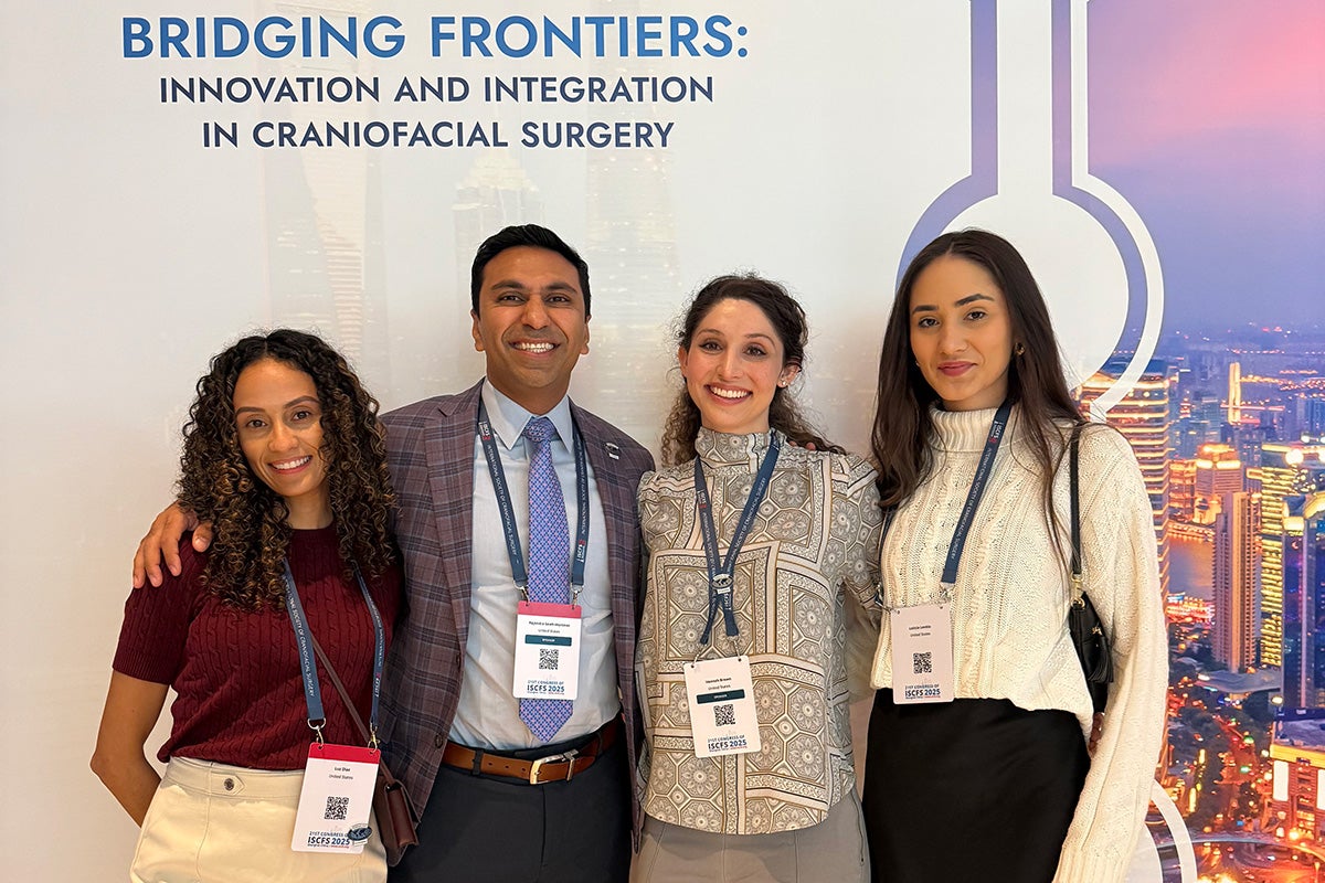 three women and a man stand side by side to pose for photo in front of conference banner