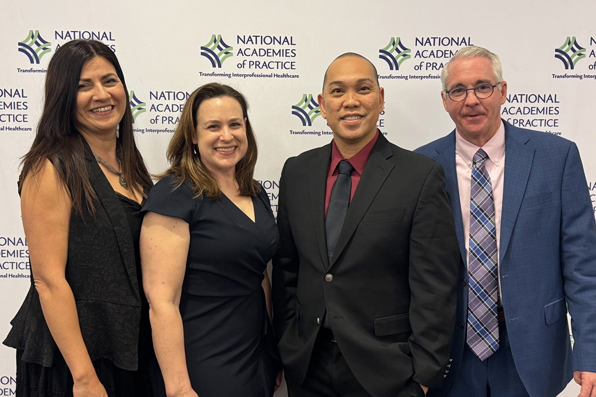 two women and two men wearing professional attire pose in front of back drop