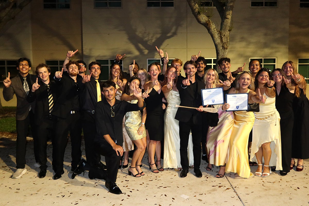 A large group of college students, dressed in formal wear, hold up two certificates and No. 1 signs with their fingers