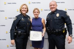 UCF Police Chief Robbin Griffin-Kitzerow and Deputy Chief Scott Freeman stand with a woman as she holds her promotion certificate in front of a UCF Public Safety backdrop.
