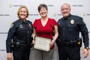 UCF Police Chief Robbin Griffin-Kitzerow and Deputy Chief Scott Freeman stand with a woman as she holds her promotion certificate in front of a UCF Public Safety backdrop.