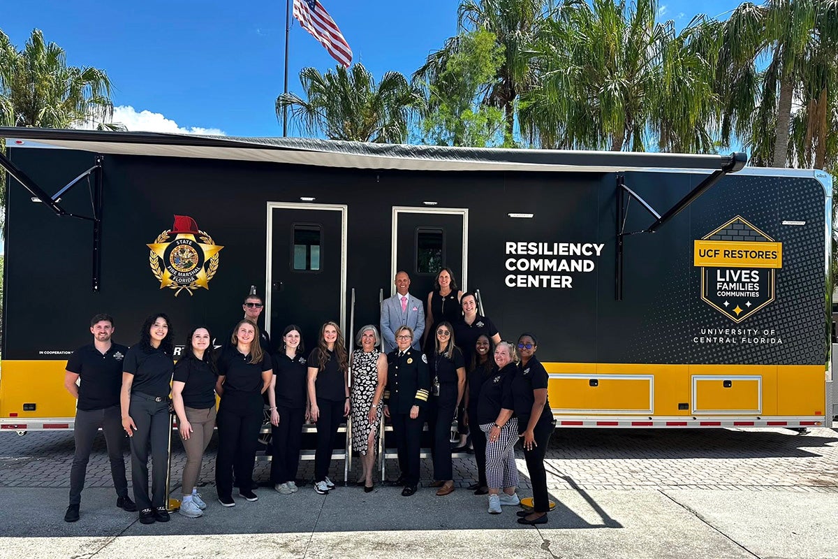 Roughly a dozen people standing shoulder to shoulder in front of black and yellow mobile trailer with words on the side that read: Resiliency Command Center.