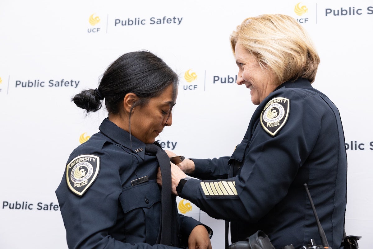 A new UCF Police Department officer stands in uniform as UCF Police Chief Robbin Griffin-Kitzerow pins her badge during a swearing-in ceremony.