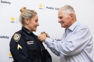 UCF Police Department Corporal Melissa Guadagnino stands in uniform as her father pins her badge during a ceremony.