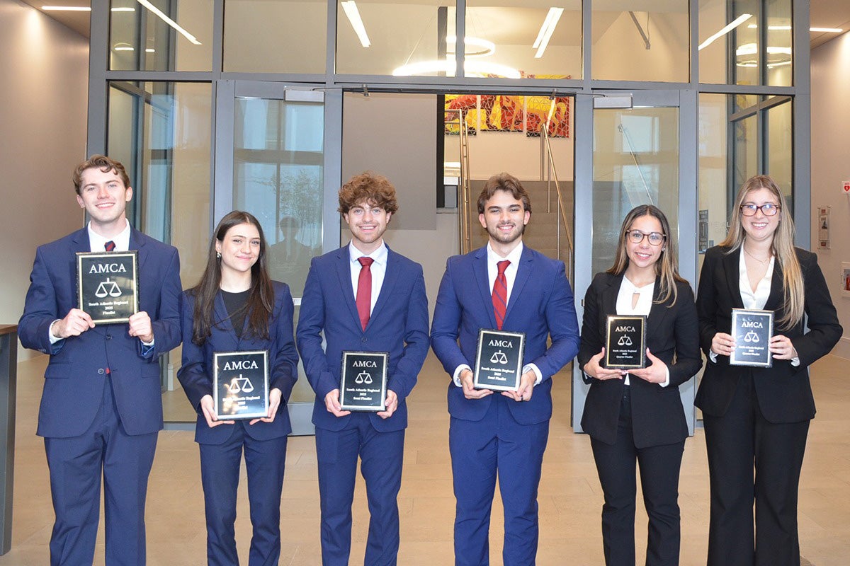 Six male and female college students dressed in suits hold plaques while standing in front of glass doors