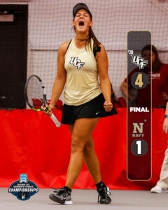 Score graphic showing UCF 4 Navy 1 alongside UCF women's tennis player wearing gold shirt and black skirt, holding a racket in right hand and clenching left fist while shouting on the court.