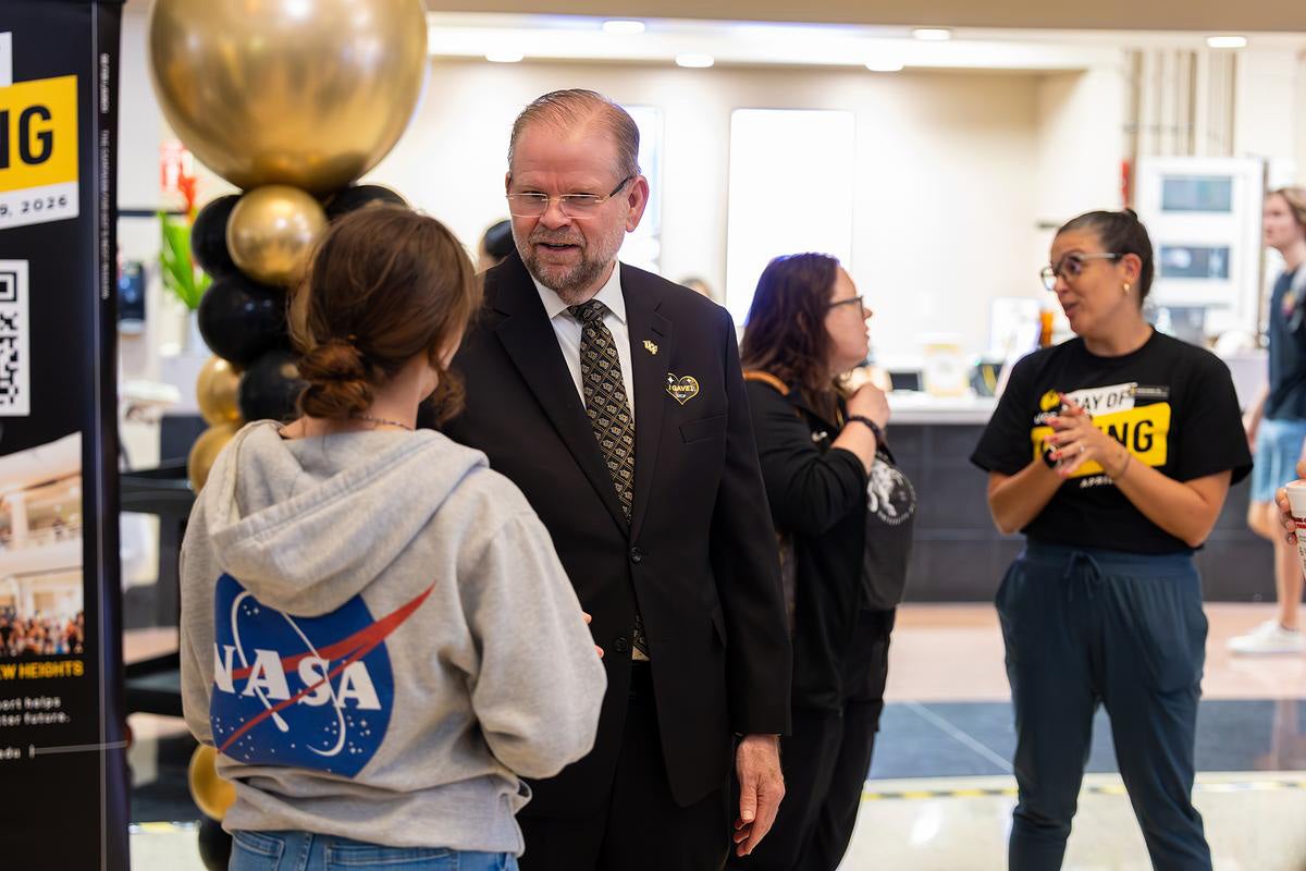 President Alexander N. Cartwright, wearing a suit and tie, speaks to a female college student wearing a gray NASA hoodie in atrium of UCF Student Union.