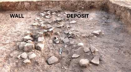 Archaeological excavation showing a mudbrick wall and a deposit of broken pottery and debris preserved at Kurd Qaburstan, with “WALL” and “DEPOSIT” labels marking key features.
