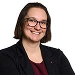 Woman wearing glasses and a dark blazer smiles in a professional headshot against a white background.