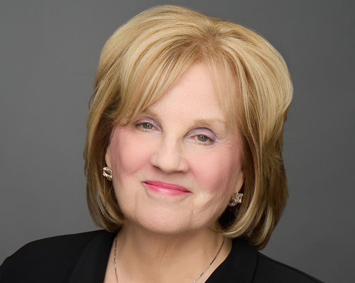 Headshot of blonde woman wearing black top in front of a gray backdrop