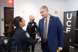 A man in a suit shakes hands with a UCF police officer during a ceremony, while another officer stands in the background.