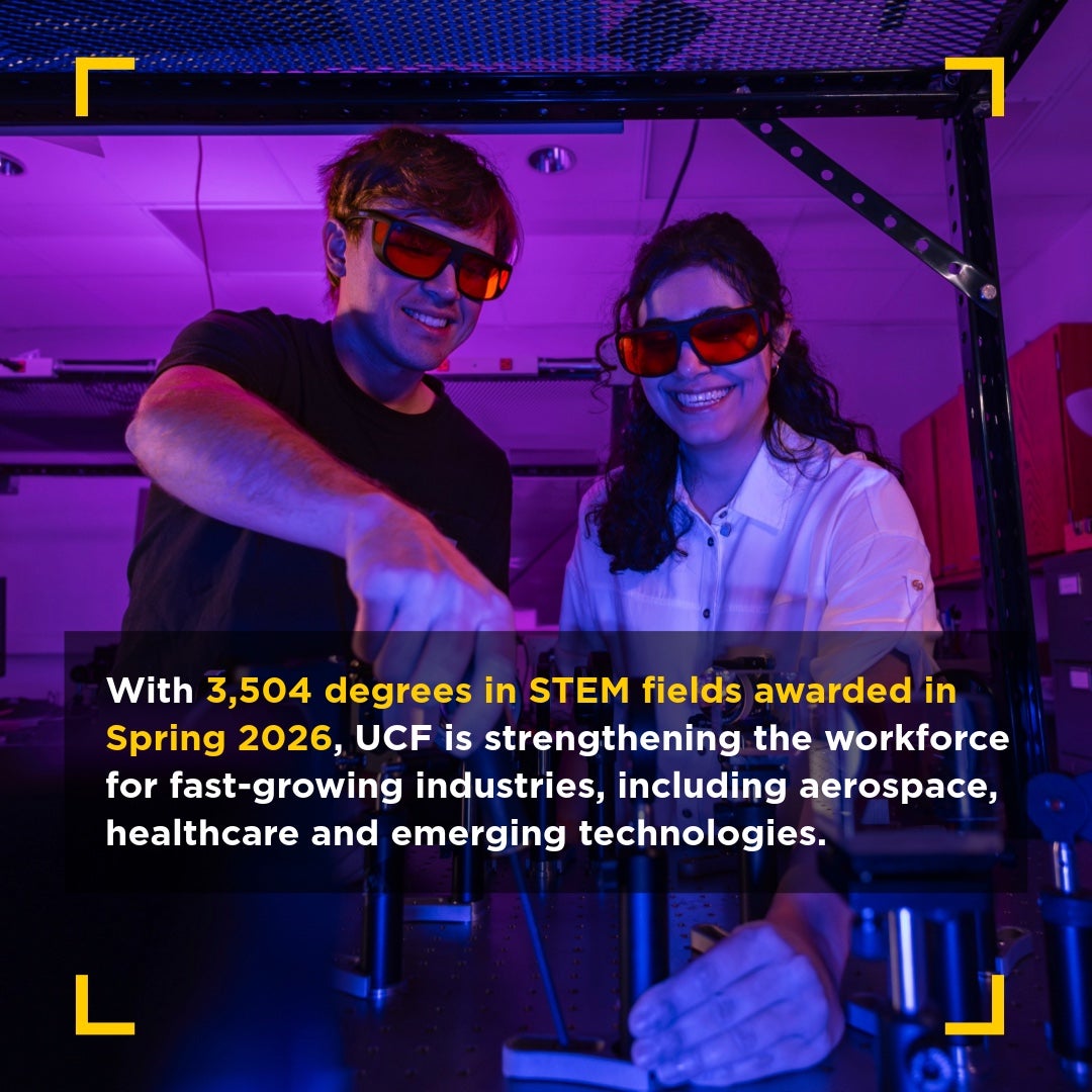Two students wearing protective glasses work together in a lab with equipment under purple lighting. Overlaid text reads: "With 3,504 degrees in STEM fields awarded in Spring 2026, UCF is strengthening the workforce for fast-growing industries, including aerospace, healthcare and emerging technologies."