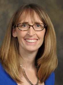 headshot of woman with dirty blonde hair, glasses and blue blouse