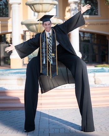 Christian Spencer wearing a grad cap and gown while wearing stilts at UCF Rosen College