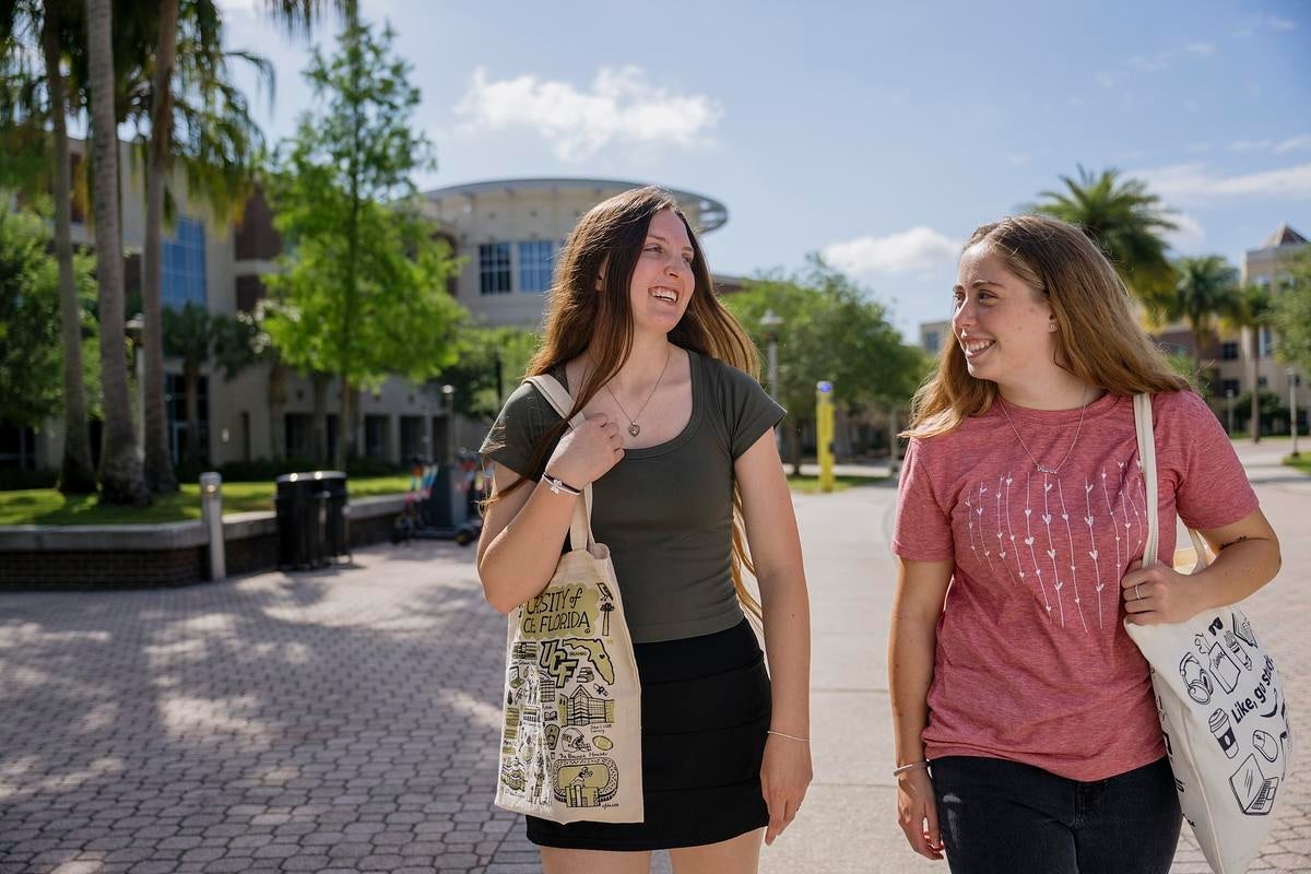 Two students wearing UCF totes walking outside on campus