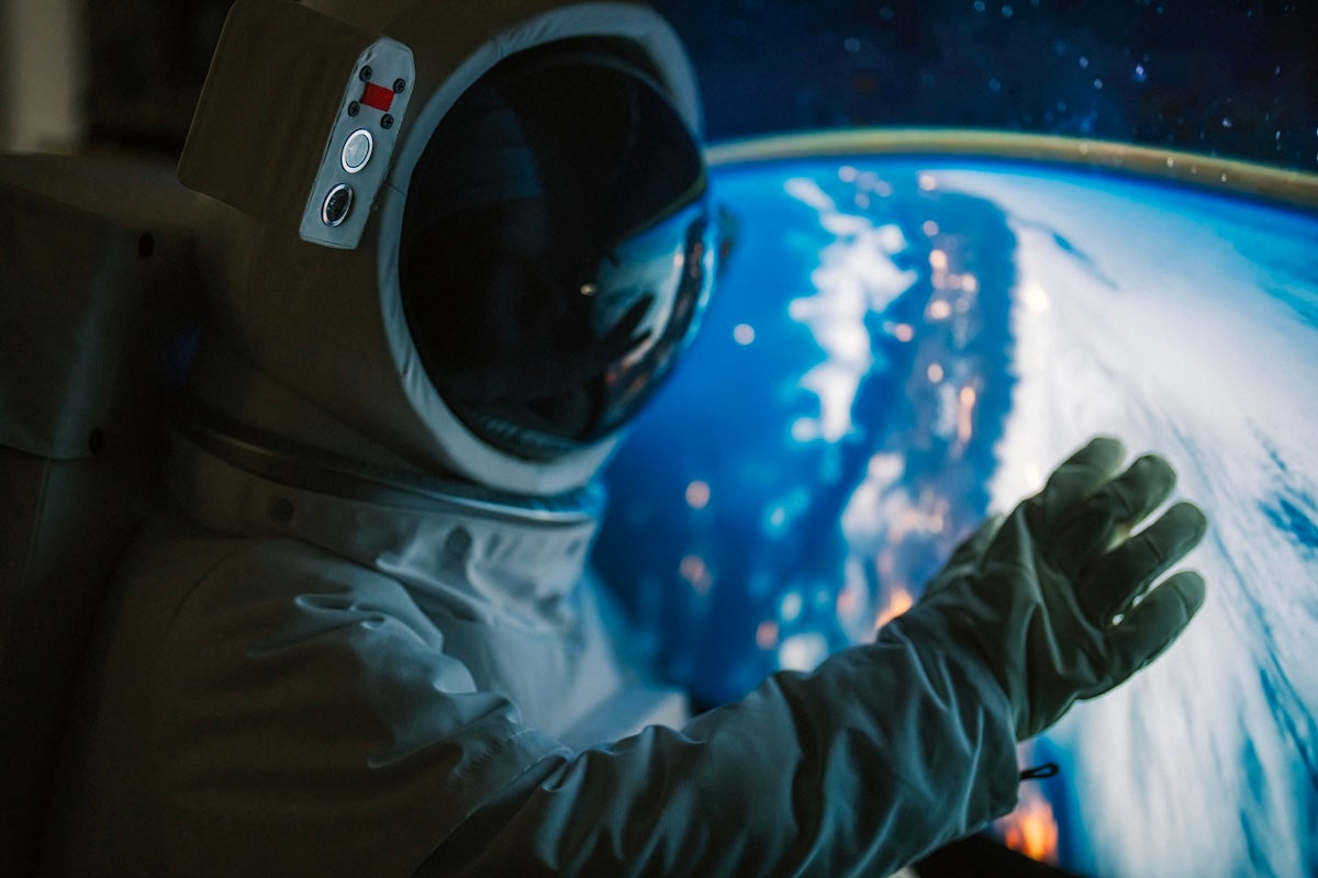 An astronaut suit displayed in front of a window overlooking Earth from space.