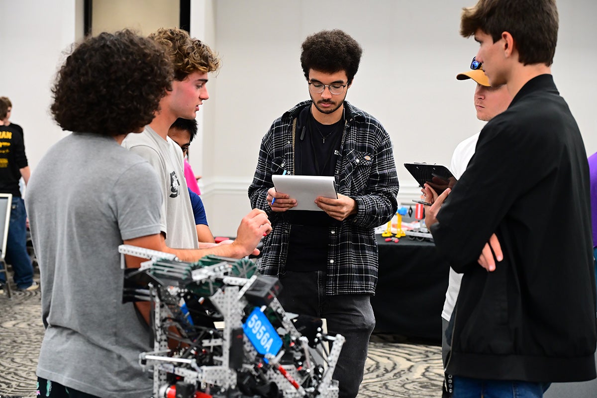 Four male college students huddle around robot for discussion in working group.