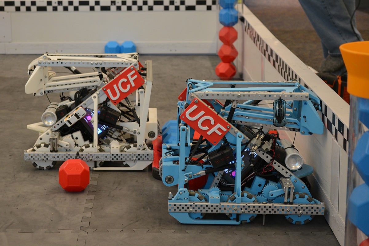 Two mechanical robots, identical in shape and structure but one white and one blue, with red and white UCF label on side.