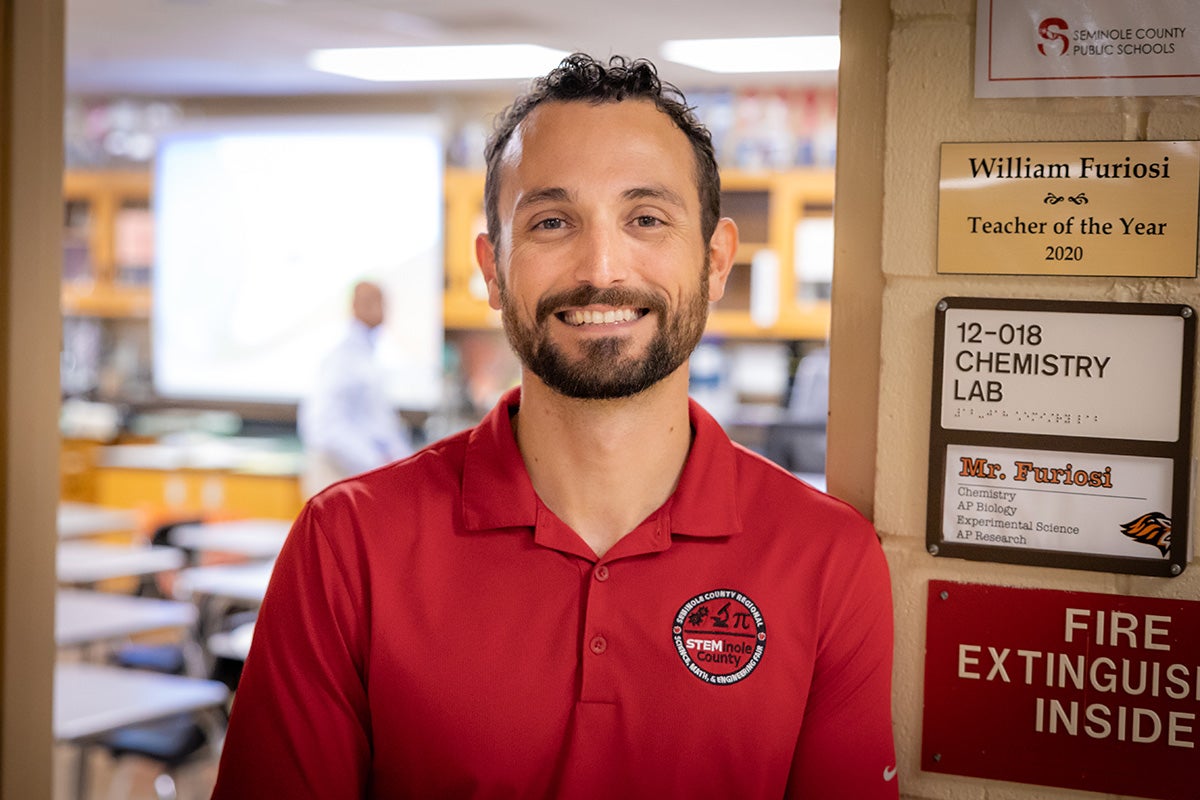 Bearded man in red polo shirt standing in doorway of high school classroom
