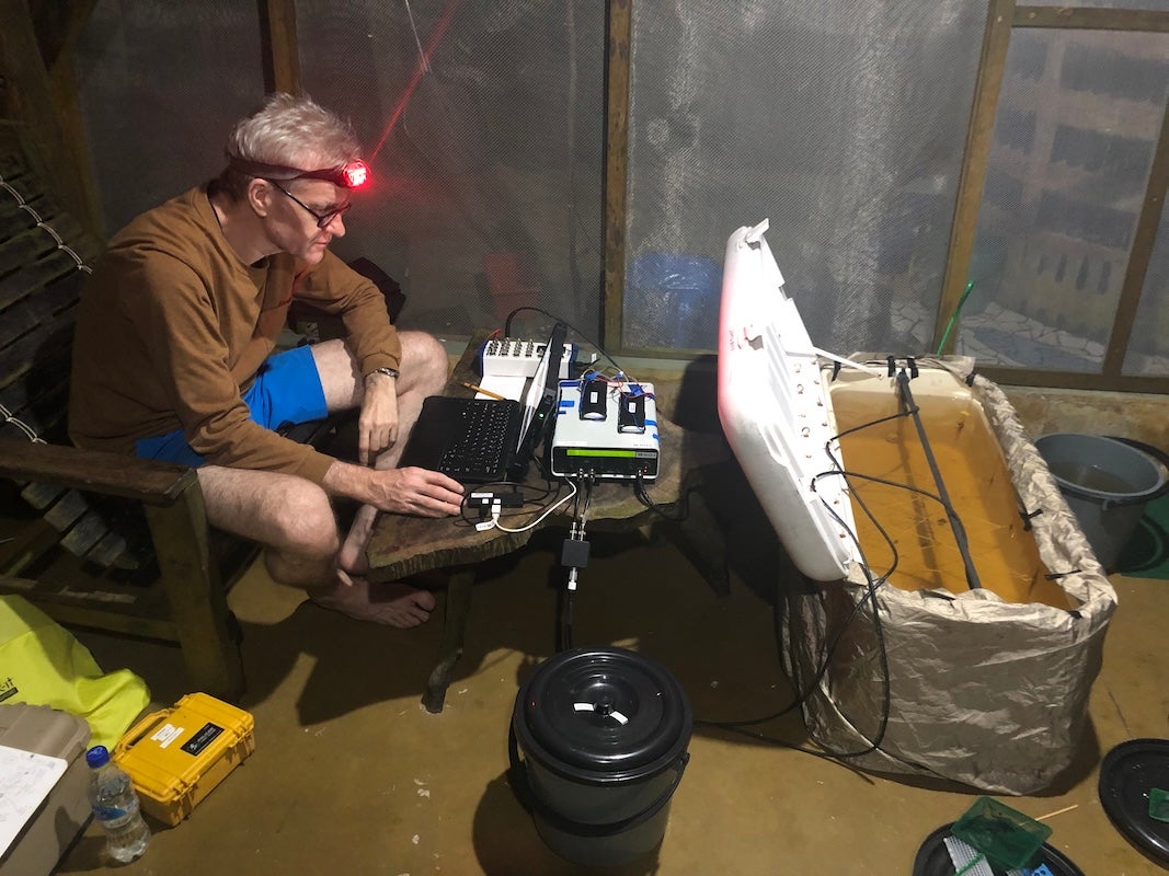 Professor William Crampton monitors recording equipment beside a water-filled tank during a nighttime field study.