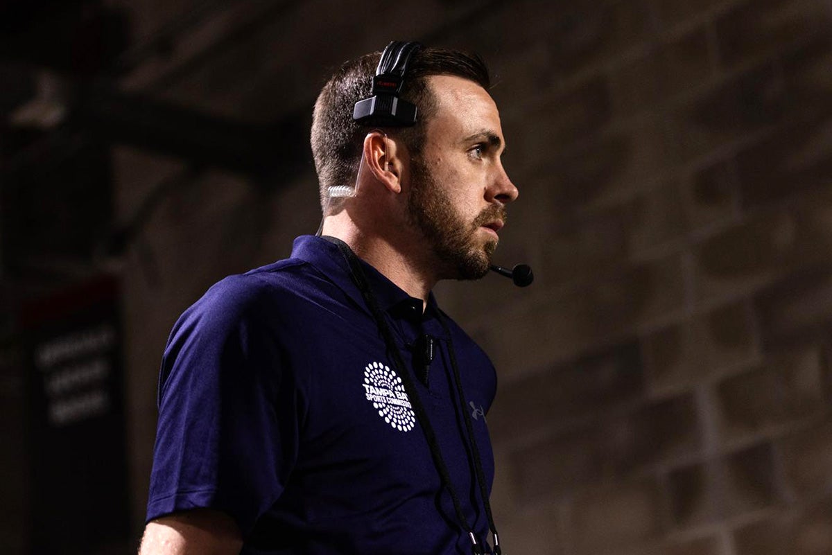 Side profile potrait of man wearing headset and polo with Tampa Bay Sports Commission logo in white on right shoulder