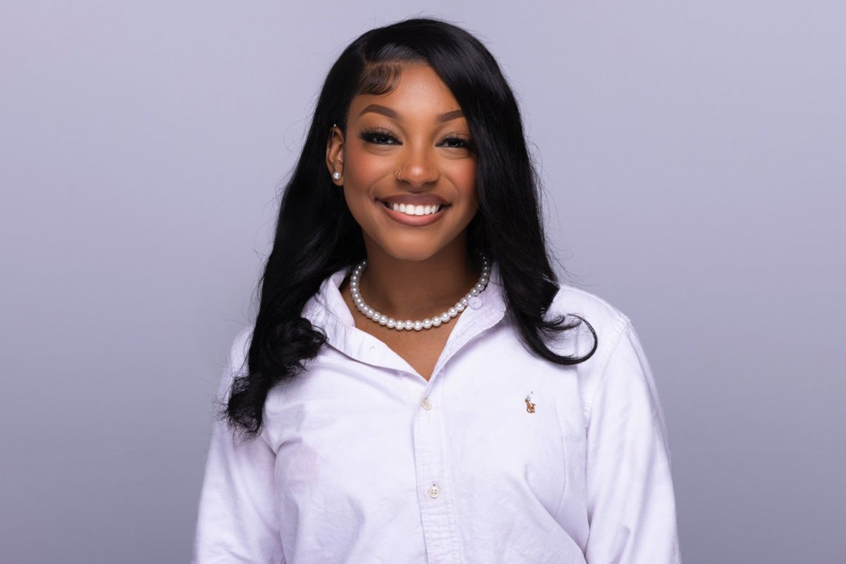 Portrait of Black woman with dark shoulder length hair wearing a white long sleeve polo shirt and necklace
