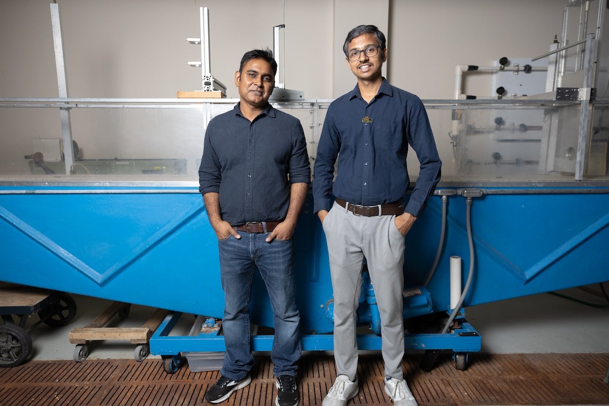 UCF associate professor Arvind Singh stands with another researcher in front of a large hydraulic flume used to study river flow, erosion and landscape evolution.