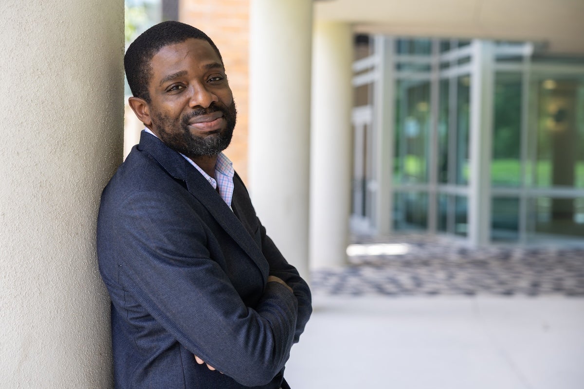 UCF electrical and computer engineering associate professor Chinwendu Enyioha stands with his arms crossed while leaning against a column outside the Engineering I building.