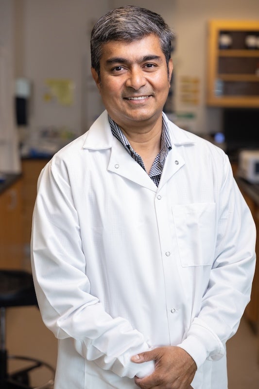 UCF materials science and engineering associate professor Mohiuddin Quadir stands in a laboratory wearing a white lab coat and smiling at the camera.