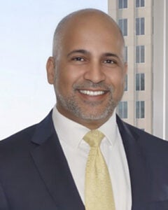 Professional head shot of bald man with stubble beard, dark suit jacket, white shirt and light yellow tie