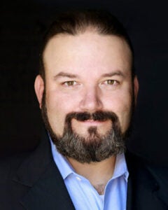 Professional head shot of bearded man with dark suit and light blue collar shirt