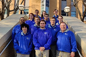 Members of UCF’s Collegiate Cybersecurity Competition Team pose on the steps of a building wearing matching blue jackets.