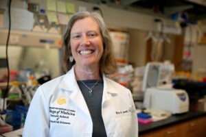 UCF infectious disease expert Mollie Jewett smiles while wearing a white lab coat in a research lab.