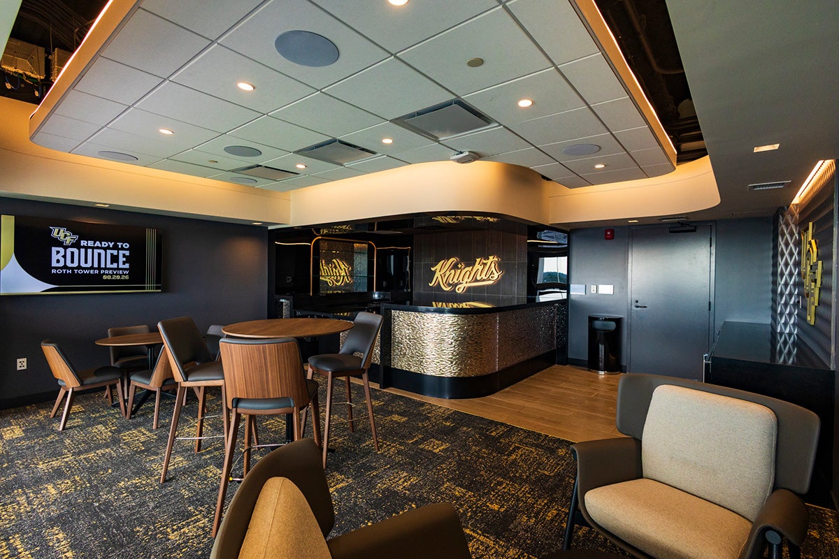empty bar space with high top chairs and tables and a Knights script word art glowing on black wall behind bar