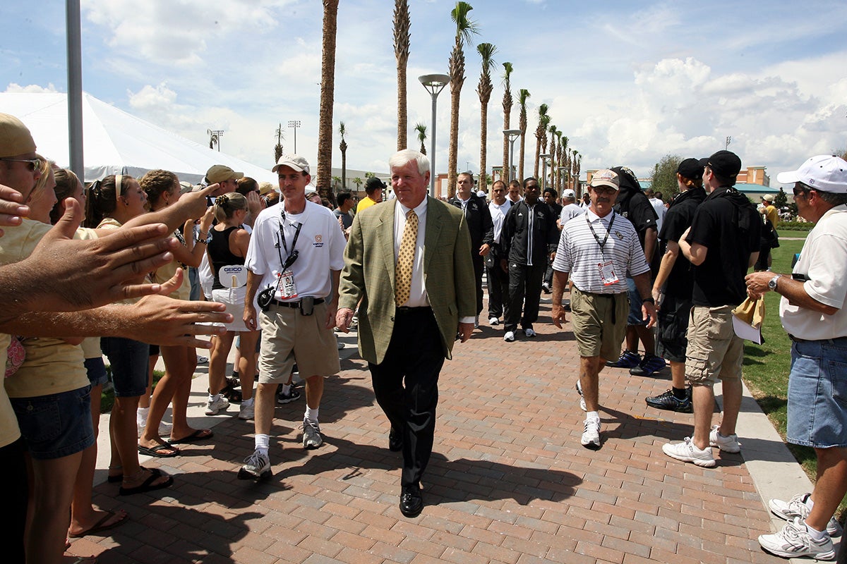 Two men walk on paved walkway while football fans stick out hands for hive fives