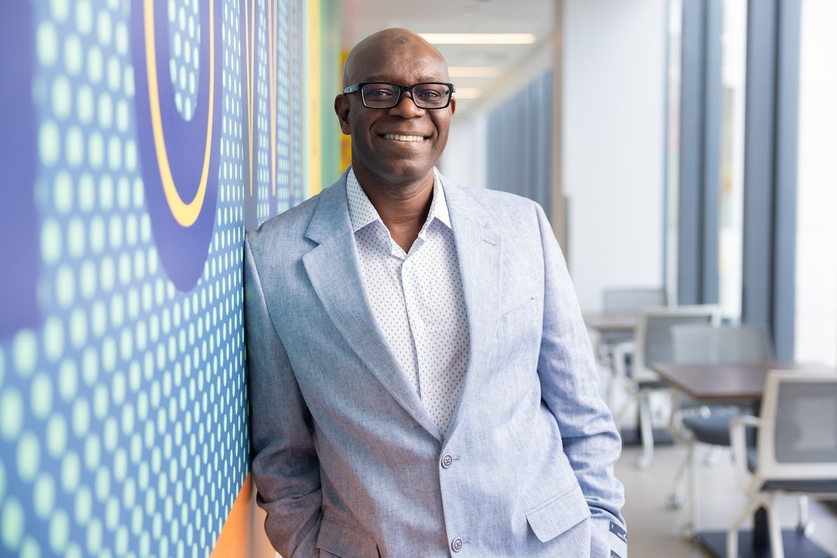 UCF Professor Abdul-Akeem Sadiq smiles for a photo while leaning against a colorful wall in a hallway at UCF Downtown.