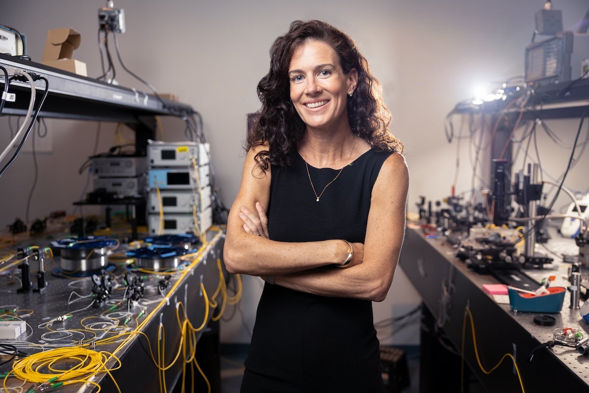 Florida Photonics Center of Excellence Endowed Professor Andrea Blanco-Redondo stands with her arms crossed in a research lab surrounded by optical equipment and cables.