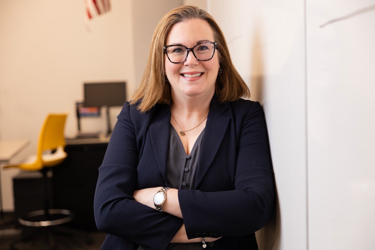 UCF Professor Claire Connolly Knox smiles, arms crossed, as she leans against a whiteboard in a classroom.