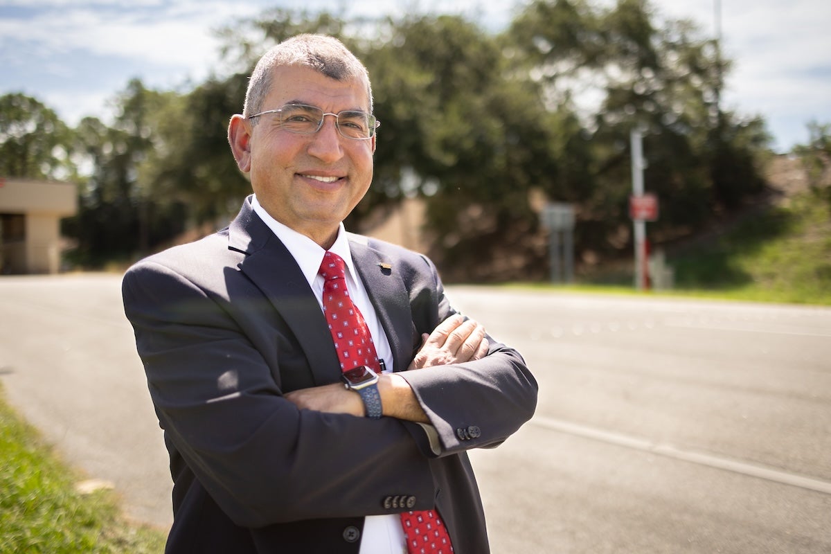 UCF Professor Haitham Al-Deek stands outdoors, arms crossed, near a roadway.