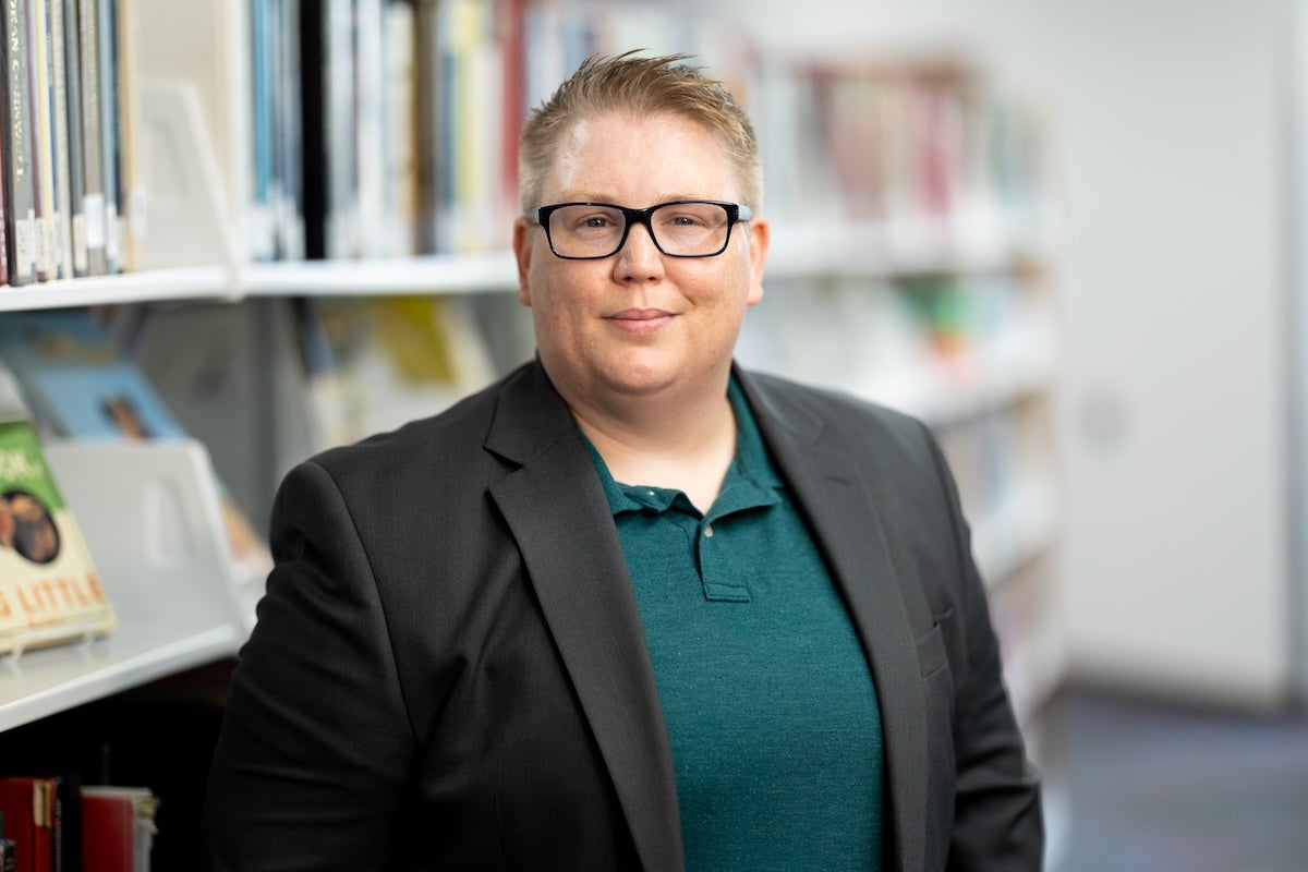 UCF Professor Mel Stanfill poses for a photo in front of bookshelves at John C. Hitt Library.