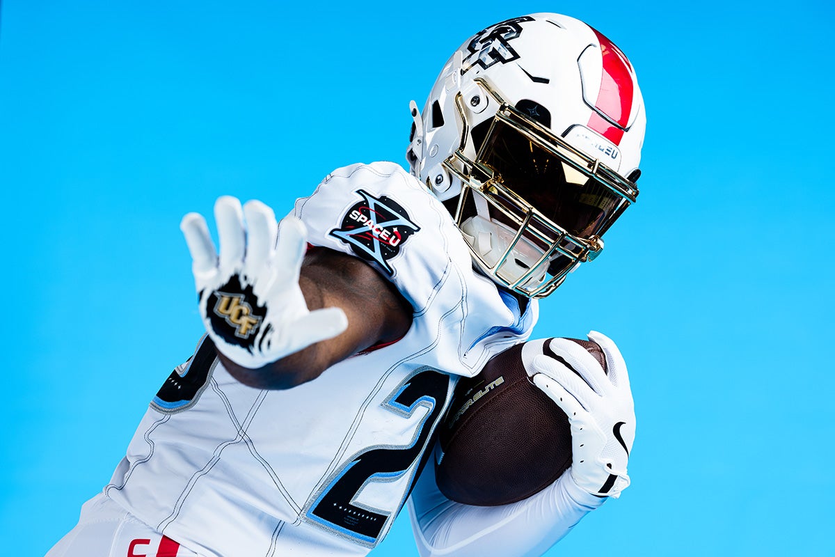 UCF football player Taevion Swint models MIssion X white uniform while cradling football in left arm