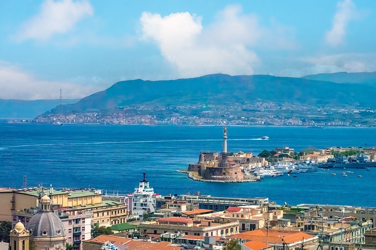 Mediterranean landscape of town and water against a backdrop of mountains and blue, cloudy sky