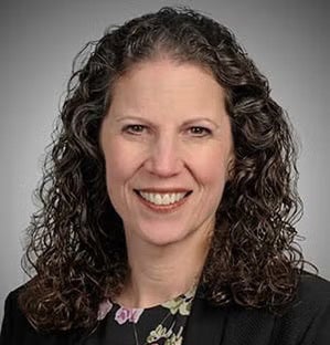 Portrait of smiling woman with dark curly hair against a gray backdrop