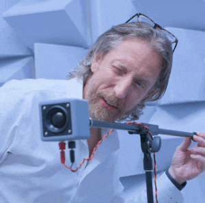 motion graphic clip of man in white sleeve shirt peering into square shaped technology device on a gray tripod
