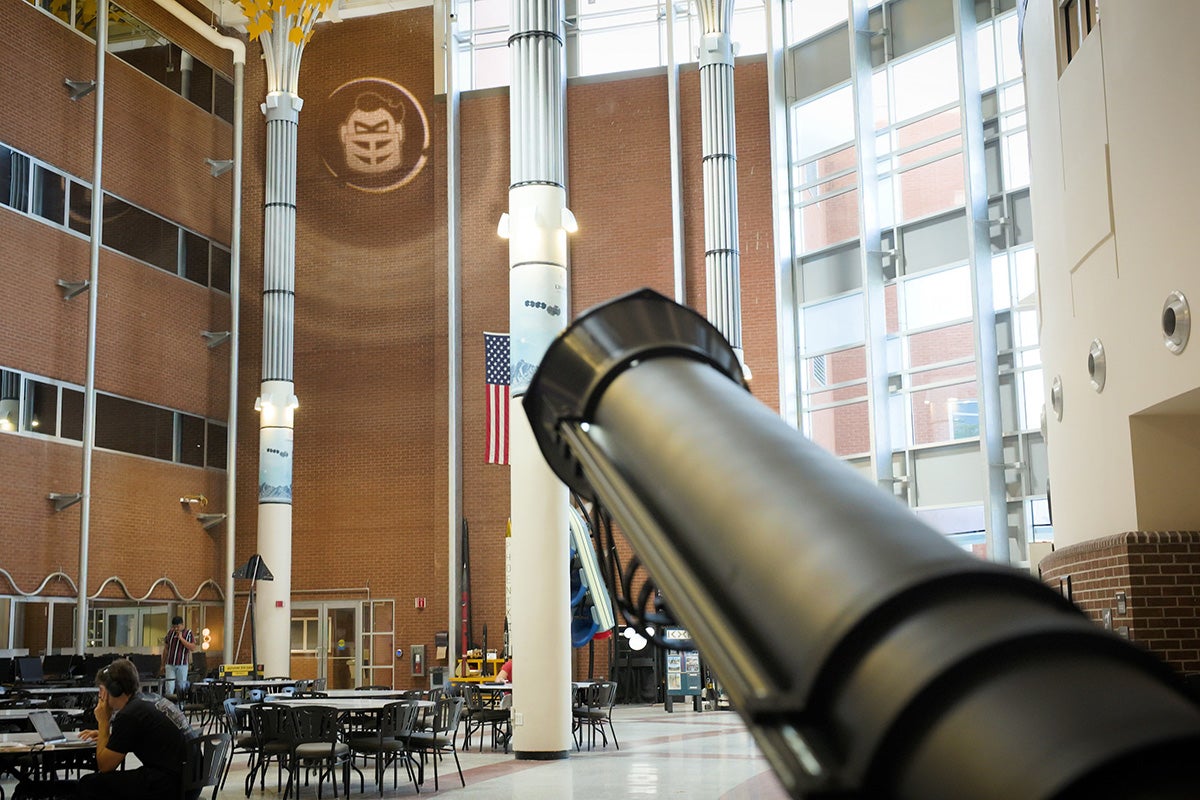 Black cylinder projection light shines Knighthead logo onto brick walls of engineering building atrium 