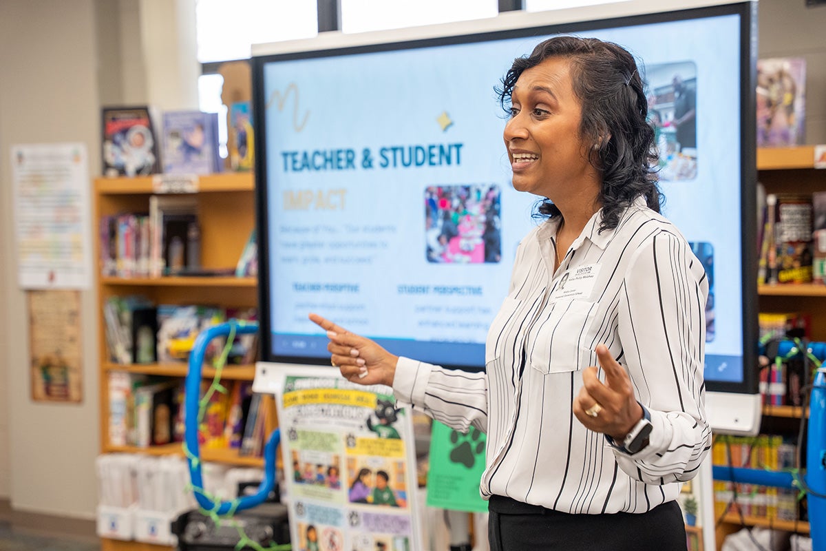 Nisha Phillip Malahoo stands and speaks in front of a digital presentation board in the media center at Pinewood Elementary.