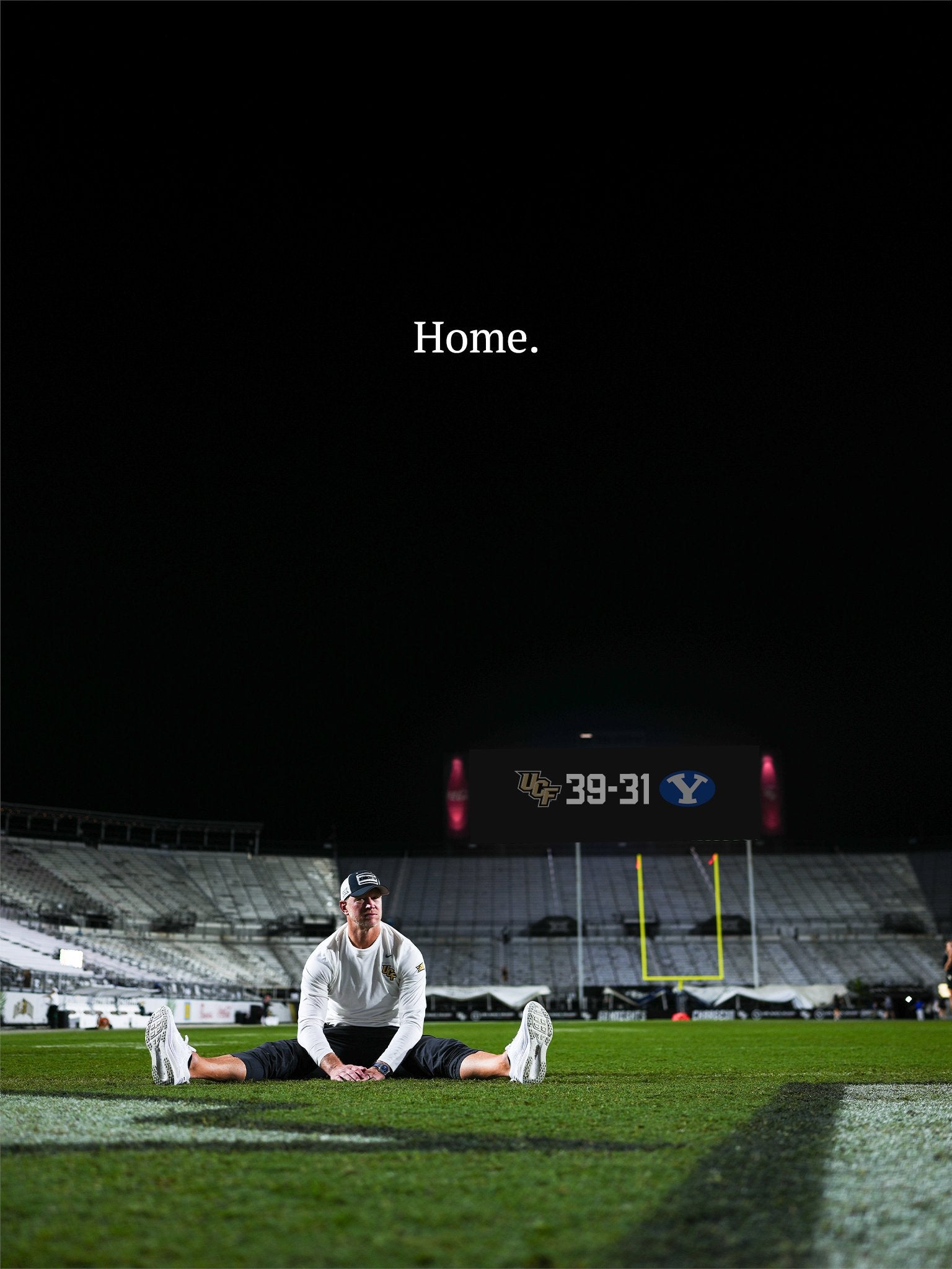 Scott Frost sits in end zone of empty stadium with the word Home written above him in white text in the night sky